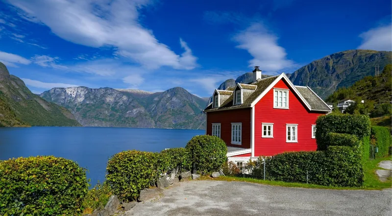 A red timber house beside the calm fjord with mountains behind