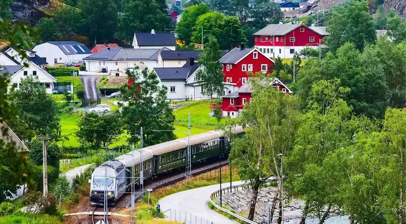 The Flåm Railway train passing red houses in the Flåm valley