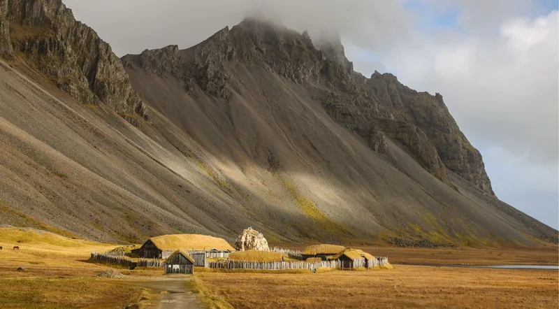 Turf-roofed Viking houses below a towering mountain